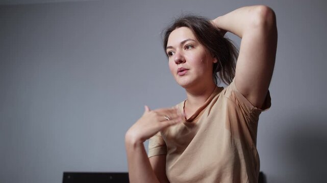 Sweaty young woman waves her hand at her face while enduring oppressive heat at home. Slow motion footage shows frustration without air conditioning.