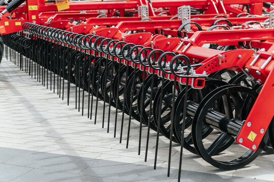 Red Agricultural Seeder With Discs And Tines Stands On Paved Surface. Modern Farming Equipment Row At Exhibition