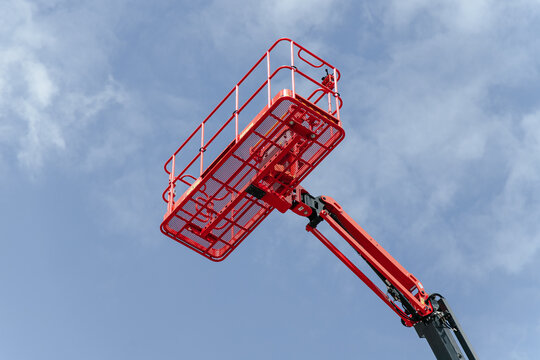 Single Red Lift Basket Rises Against A Blue Sky. Industrial Equipment Stands Ready For High Altitude Work.