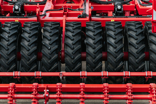 Red Agricultural Roller Features Heavy Duty Tires And Steel Frame. Farm Equipment Awaits Field Preparation Work.