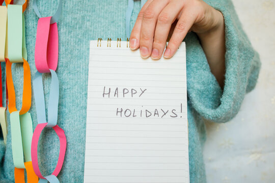 Young woman in festive Christmas look keeping in hand paper notepad with handwritten happy holiday phrase. Christmas holidays wishes, New year and party festive mood