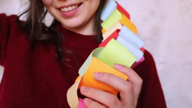 Young woman brunette in festive red Christmas sweater playing with handmade paper multicolored dopamine garland on her neck. Christmas holidays nostalgia, New year and party festive mood