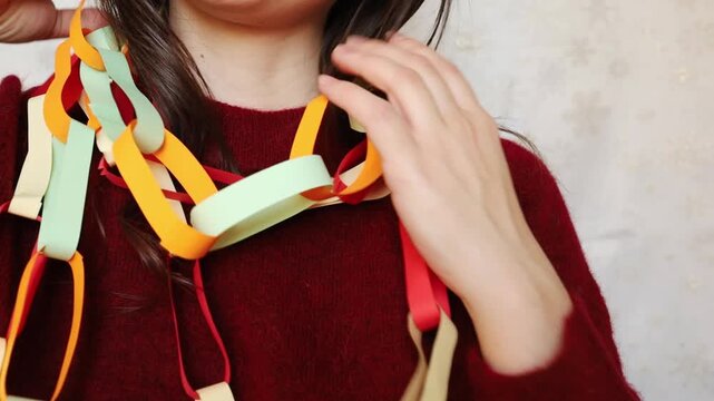 Young woman brunette in festive red Christmas sweater playing with handmade paper multicolored dopamine garland on her neck. Christmas holidays nostalgia, New year and party festive mood