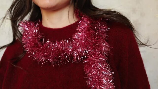 Young woman brunette in festive red Christmas sweater playing with pink sparkling tinsel on her neck. Christmas holidays, New year, sparkling vibe and party festive mood