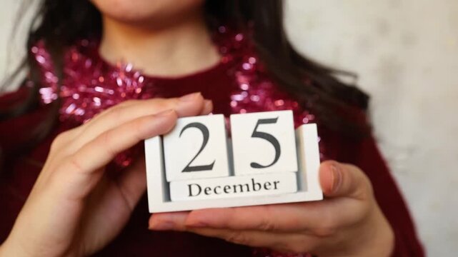 Young woman brunette in festive Christmas look keeping in hands white wooden calendar with Christmas date 25 of December close up. Christmas celebration preparation, catholic religion holiday date
