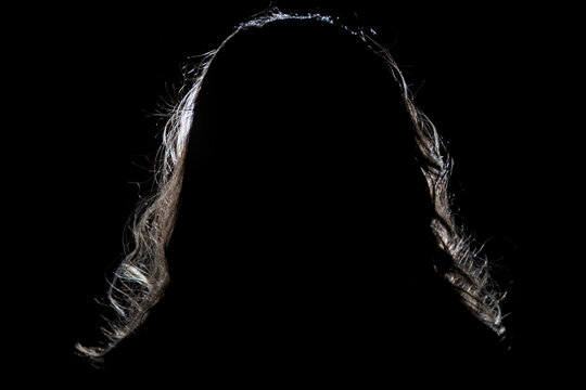 Artistic studio portrait of woman silhouette with beautiful rim lighting on her long wavy hair against dark black background.