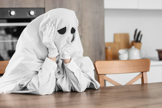 Loneliness and social anxiety, person in ghost costume sitting at kitchen table feeling sad and isolated during mental health struggle at home