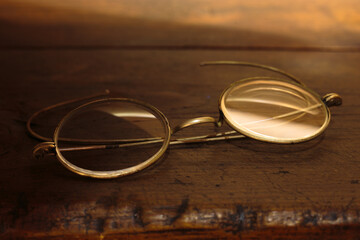 Naklejka premium Vintage spectacles resting on weathered wooden surface with warm ambient lighting. Intellectual themes