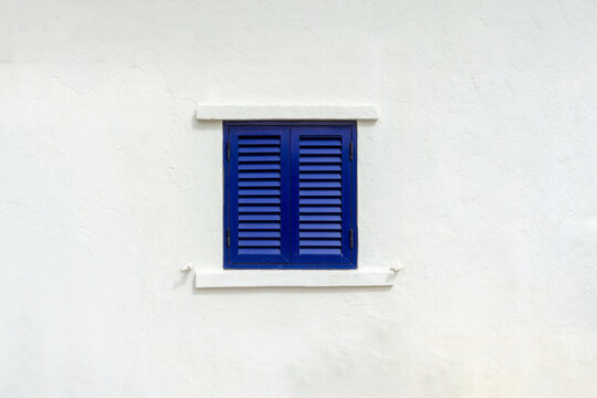 Blue wooden louvered shutters providing a striking color contrast against a textured white stucco wall, embodying traditional Portuguese architecture and coastal charm