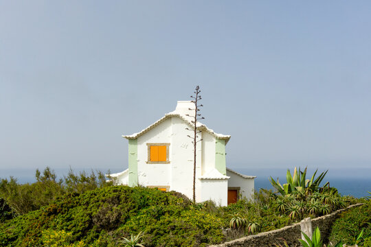 White traditional Portuguese house with orange shutters perched on a lush green cliffside overlooking the Atlantic Ocean in Azenhas do Mar, scenic seaside village retreat