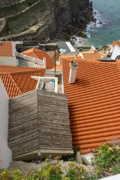 Azenhas do Mar village buildings with terracotta rooftops and traditional chimneys cascading down a steep cliffside to the Atlantic Ocean, featuring a small beach and crashing waves