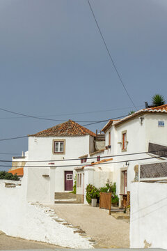 Azenhas do Mar village showing traditional white houses with terracotta roofs and a winding street under a cloudy sky, capturing Portuguese coastal architecture