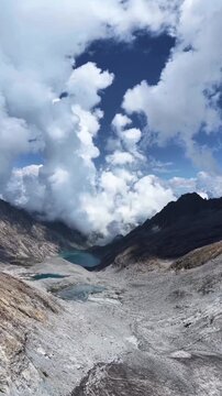 clouds over the mountains, Dramatic white clouds billow dramatically over rugged rocky mountains and small alpine lakes nestled within a high elevation valley under a deep blue sky.