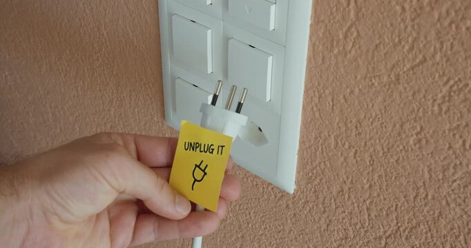 Hand unplugs an electrical plug from a power outlet, representing energy saving and reduced electricity use.