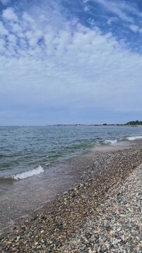 Vertical portrait of a natural gravel beach with soft waves and cirrocumulus clouds over the blue sky in Kurobe, Toyama, Japan. Perfect for environmental tourism and mobile backgrounds.