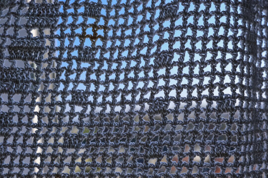Close-up of a black fishing net against the sky with sea and distant shore behind