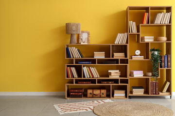 Interior design and home library, wooden bookshelves with books and decor against a yellow wall in a modern living room with minimalist furniture © Pixel-Shot