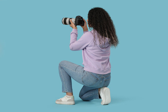 Photography hobby and creative career, young woman with curly hair using a professional dslr camera to take pictures while kneeling on blue background