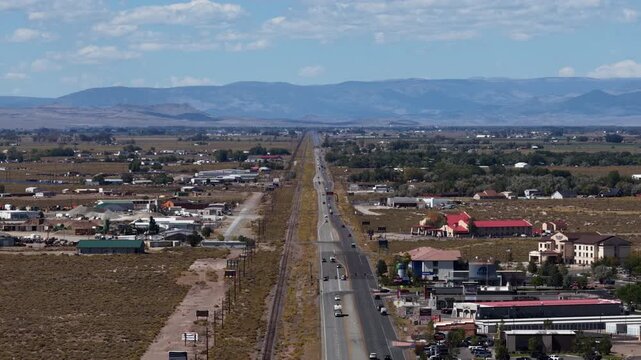 Aerial of US highway 285 and parallel railroad tracks running through the town of Alamosa Colorado with mountains in the background under a sunny sky