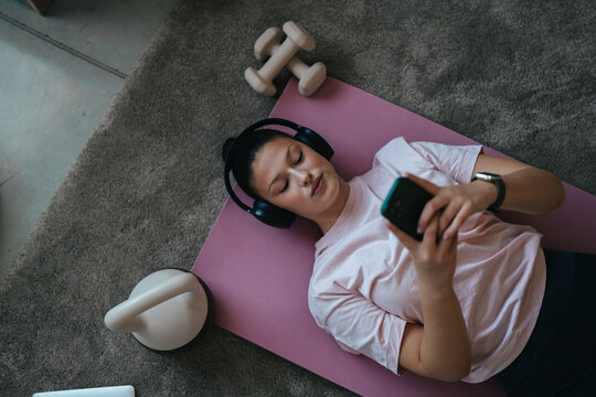 Young woman relaxing on yoga mat using smartphone