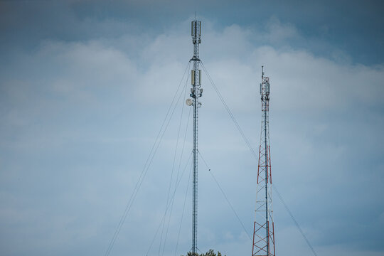 Tall communication towers with antenna arrays and support cables rising against a dramatic cloudy blue sky in a minimal telecommunications infrastructure landscape
