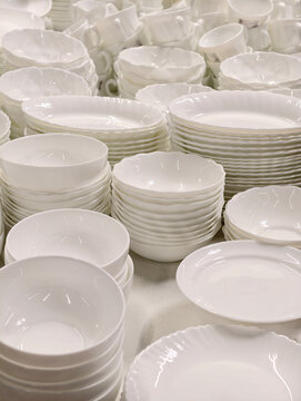 White ceramic plates and cups of various shapes displayed on supermarket shelves forming a simple assorted kitchenware set designed for everyday use and retail sale