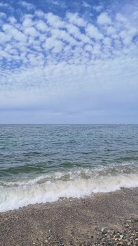 Vertical portrait of white cirrocumulus clouds spreading across a blue sky over the calm sea horizon in Toyama, Japan. Perfect for minimalist mobile backgrounds and autumn banners.