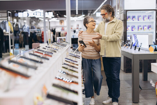 Mature couple choosing new mobile phone in electronics store, shopping for modern technology and communication
