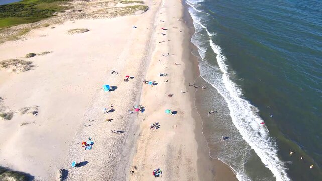 Breaking waves run beside a broad Virginia beach backed by low vegetated dunes.
