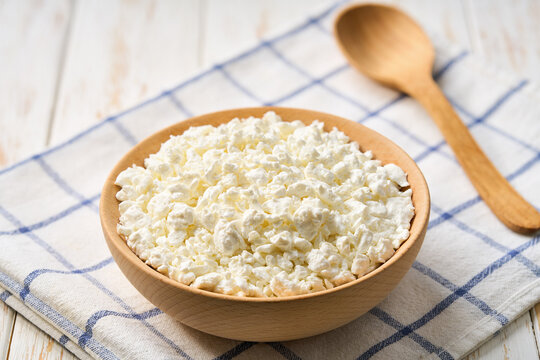 Fresh cottage cheese in a wooden bowl on a white table, selective focus.