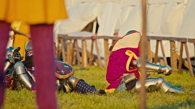 Several armored knights collapse together onto green grass. Fierce medieval tournament battle ends with heavy fighters tangled in chaotic pile wearing bright surcoats and metal plates.