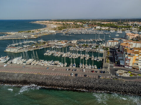Aerial view of Cap d&rsquo;Agde marina on the Mediterranean coast in Occitanie, H&eacute;rault, France, with yachts, waterfront buildings, and a sunny seaside holiday atmosphere.