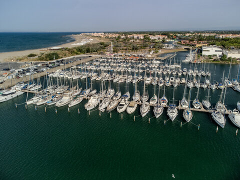 Aerial view of Cap d&rsquo;Agde marina on the Mediterranean coast in Occitanie, H&eacute;rault, France, with yachts, waterfront buildings, and a sunny seaside holiday atmosphere.