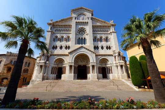 Main facade of Monaco Cathedral with rose window, arched portals flanked by palm trees, Monaco-Ville, French Riviera