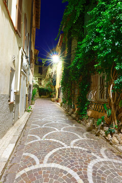 Cobblestone alley at night with fan-shaped paving pattern, glowing street lamp in Antibes Old Town, French Riviera, France