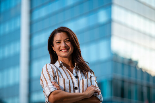 Confident businesswoman smiling with arms crossed in front of skyscraper