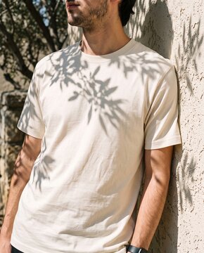 A young man wearing a blank off-white crewneck t-shirt outdoors with natural sunlight and leaf shadows, ideal for apparel design mockup.