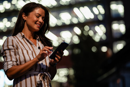Woman smiling using smartphone at night in city