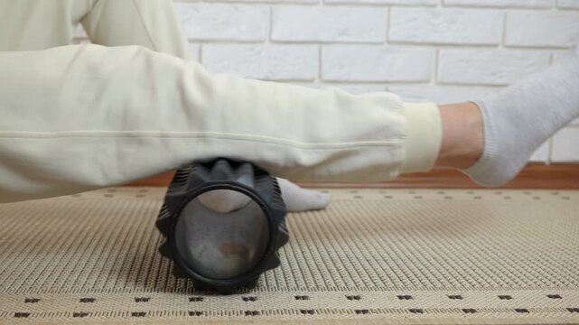 Woman massaging calf muscle with foam roller. Close-up view of a person performing myofascial release on their lower leg using a black foam roller, effectively easing muscle tension
