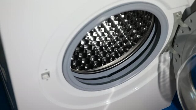 Person loading laundry into a washing machine. Close-up of a person's hand putting dirty clothes into the drum of a modern front-loading washing machine, preparing the appliance for a wash cycle