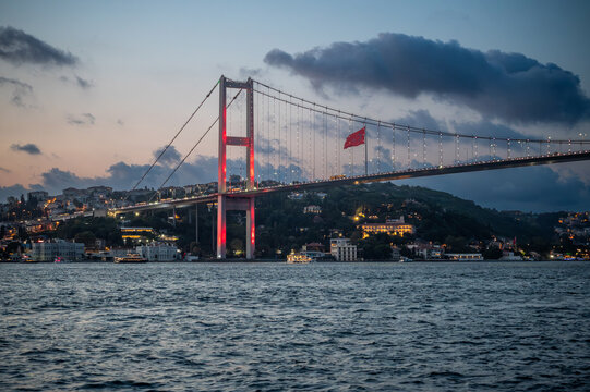 Istanbul,turkey,august 4, 2025. Bosphorus bridge spanning across the strait at twilight, city lights illuminating the european side and a turkish flag flying