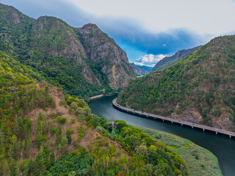 River gorge with a road viaduct below forested cliffs. Vehicles follow the water around a bend between rocky slopes under low clouds.