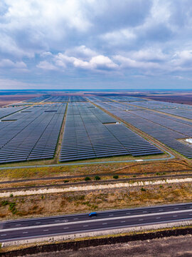 Photovoltaic installation, aerial view of solar panels and moving van. A blue vehicle travels on a paved highway adjacent to expansive rows of dark energy collectors.