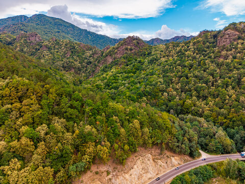 Mountain landscape, high angle shot of winding road through forest. Hilly terrain featuring diverse tree foliage and an asphalt highway carrying moving automobiles.