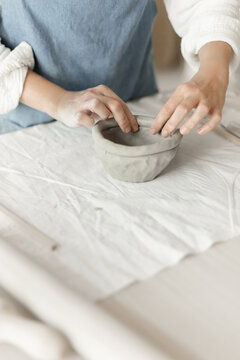Woman potter meticulously shaping clay in a studio setting, demonstrating a creative and focused approach, captured in a close-up side view, the scene showcases.