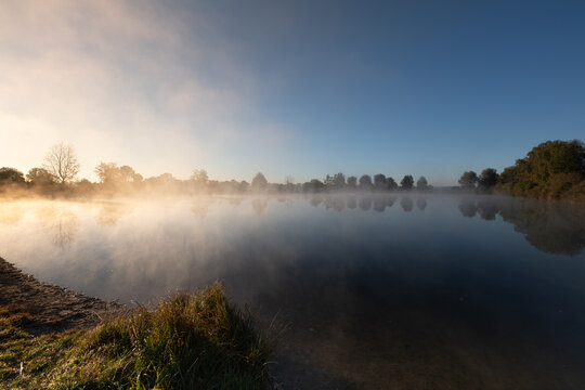 A landscape with a lake. The sun is rising. Fog drifts across the water.