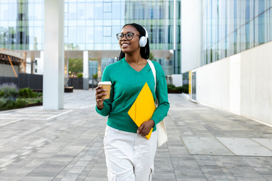 Smiling black businesswoman walking with coffee and files in a business center