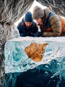Curious hikers looking at dry autumn leaf frozen in crystal clear blue ice during a winter outdoor expedition