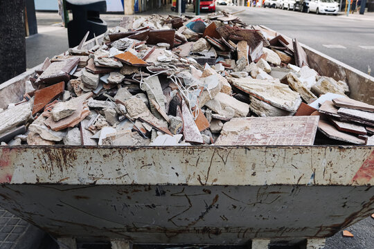 Construction debris in metal container. Broken tiles and concrete rubble. Renovation waste pile. Demolition materials and discarded fragments. Urban cleanup area. Industrial recycling background.