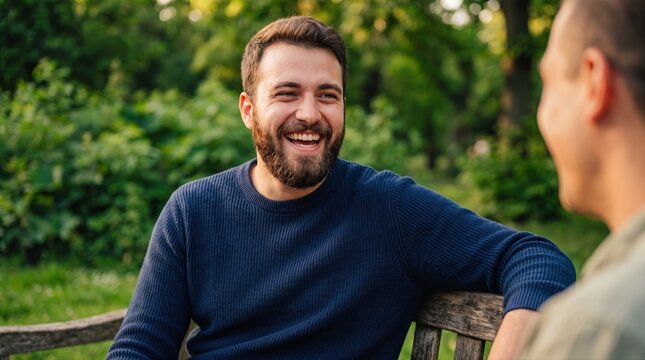 Smiling man laughing with a companion on a park bench, expressing friendship, outdoor leisure, and a joyful social moment